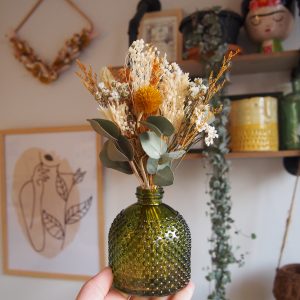 fiole verte avec bouquet de fleurs séchées oranges et blanches