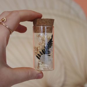 mini tube transparent avec un bouchon en liège avec des fleurs blanches et une fougère verte